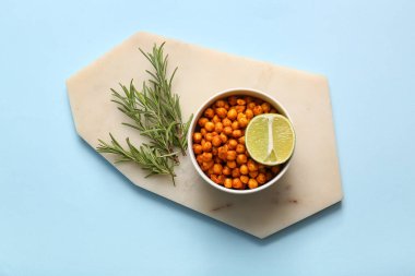 Bir kase lezzetli kızarmış bezelye, limon ve dereotlu mavi arka planda.