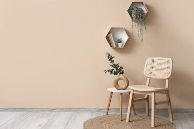 Kahve masalı rahat ahşap sandalye, okaliptüs dalları vazosu ve bej duvarın yanındaki ev bitkileri.