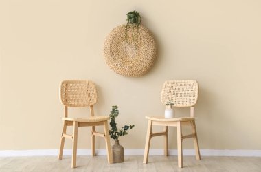 İçinde okaliptüs dalları ve bej duvarın yanında puf bulunan rahat ahşap sandalyeler.