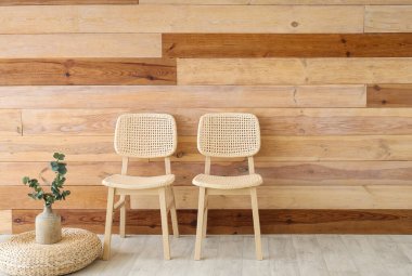 İçinde okaliptüs dalları olan rahat sandalyeler ve tahta duvarın yanında puf.