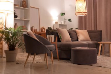 Akşamları gri kanepe, koltuk, puf ve parlayan lambalar olan modern oturma odasının içinde.