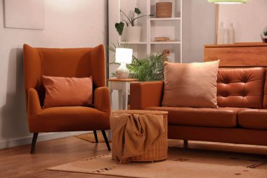 Akşamları kahverengi kanepesi, koltuğu, raf ünitesi ve parlayan lambası olan modern oturma odasının içinde.