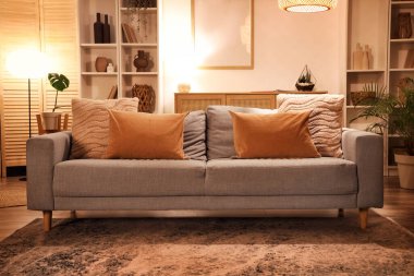 Gri kanepeli, raf üniteli ve akşamları parlayan lambalı modern oturma odasının içi.