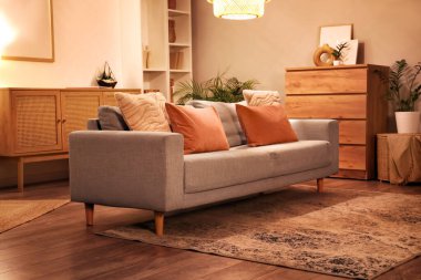 Gri koltuklu modern oturma odası, çekmeceler, raf ünitesi ve akşamları parlayan lamba.