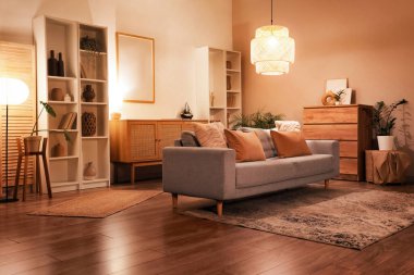 Gri kanepeli modern oturma odasının içi, çekmeceler, raf üniteleri ve akşamları parlayan lambalar.