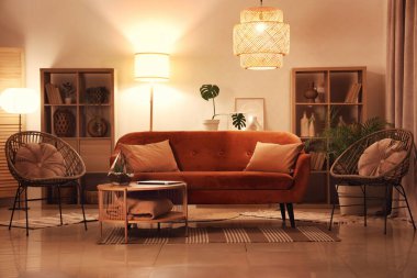 Modern oturma odasının içinde kırmızı kanepe, raf üniteleri, koltuklar ve akşamları parlayan lambalar.