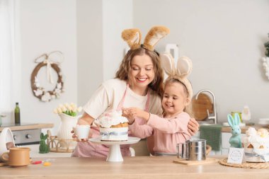 Mutlu anne ve tatlı kızı tavşan kulaklı evde paskalya pastası süslüyorlar.