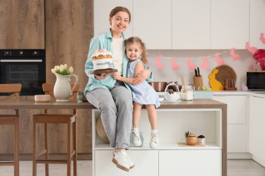 Mutlu anne ve tatlı kızı yeni pişmiş Paskalya pastasıyla mutfaktaki masada oturuyorlar.