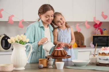 Mutlu anne ve tatlı kızı mutfaktaki yeni pişmiş Paskalya pastasına tatlı sos döküyorlar.