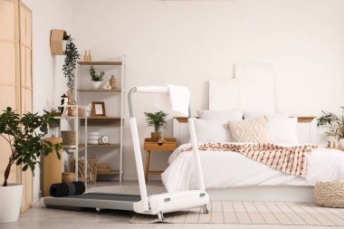 Koşu bandı, raf üniteleri ve bitkilerle aydınlık yatak odasının içinde.