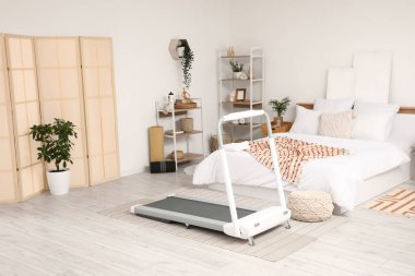 Koşu bandı, raf üniteleri ve bitkilerle aydınlık yatak odasının içinde.