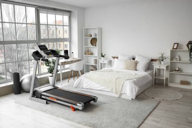 Hafif yatak odasının içinde koşu bandı, masa ve raf üniteleri var.