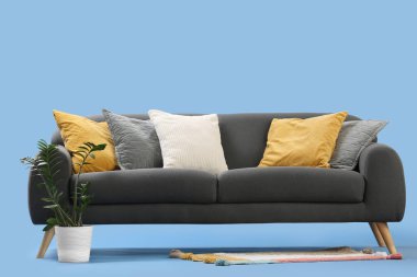 Mavi arka planda rahat yastıkları ve çiçekleri olan şık gri kanepe.