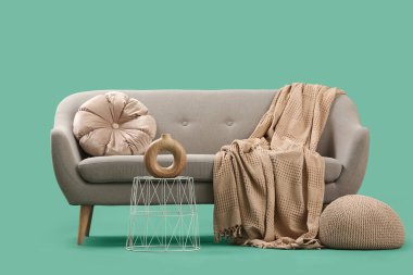 Yeşil arka planda battaniyeli, yastıklı ve sehpalı şık gri kanepe.