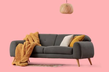 Pembe arka planda rahat yastıkları ve battaniyesi olan şık gri kanepe.