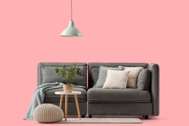 Şık gri kanepe, puf ve pembe arka planda bitki örtüsü olan kahve masası.