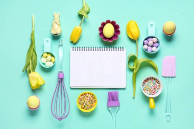 Tarifler, pişirme araçları, Paskalya yumurtaları ve renk arkaplanı üzerine renkli serpiştirmeler için boş defter içeren kompozisyon