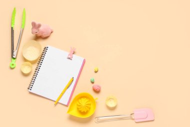 Boş tarif kitabına, fırın araçlarına ve renk arkaplanındaki Paskalya dekoruna sahip kompozisyon