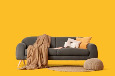 Yastıkları, battaniyesi, dergisi ve sarı arka planı olan rahat siyah kanepe.