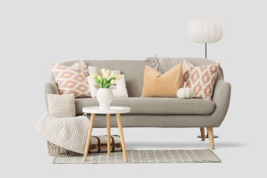 Yastıklı rahat gri kanepe, sehpa ve beyaz arka planda yer lambası.