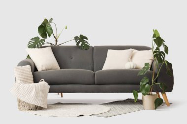 Beyaz arka planda yastıkları, çiçekleri ve sepeti olan rahat siyah kanepe.