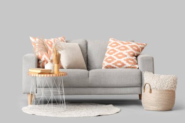 Yastıklı rahat kanepe, kahve masası ve gri arka planda sepet.