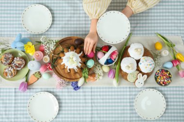 Kadın eli tabağı tutuyor ve Paskalya kutlaması için sofraya yumurta koyuyor. Üst görünüm