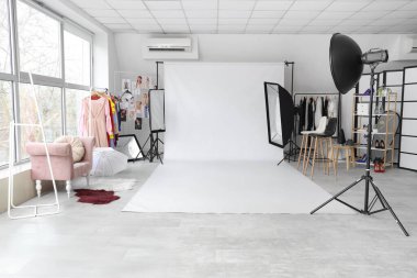 Profesyonel teçhizatı ve elbise askısı olan şık bir fotoğraf stüdyosunun içinde.