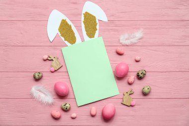 Kağıt tavşan kulaklı, tüylü ve pembe ahşap arka planda Paskalya yumurtalı boş bir kart.