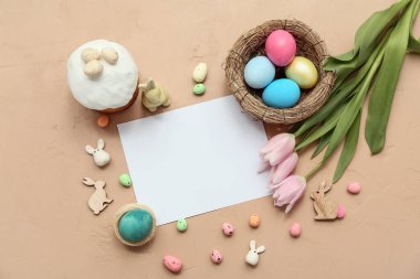 Paskalya yumurtaları, tatlı pasta, tavşanlar ve kahverengi arka planda güzel lale çiçekleri olan boş bir kart.