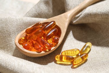 Ahşap kaşık, balık yağı kapsülleri kumaşta, yakın plan.