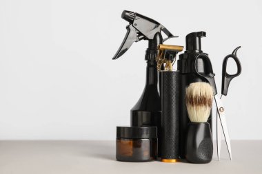 Makasla modern budayıcı, tıraş fırçası, şişeler ve hafif arkaplanda kozmetik ürünler.