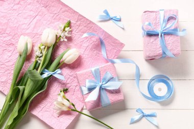 Çiçekli pembe hediye kutuları, beyaz ahşap arka planda ambalaj kağıdı ve kurdele. Uluslararası Kadınlar Günü