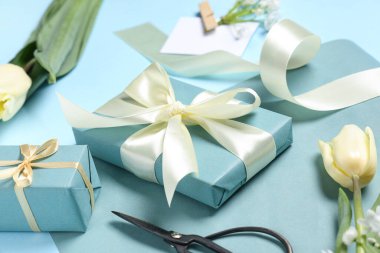 Çiçekli hediye kutuları, mavi arka planda ambalaj kağıdı ve kurdele. Uluslararası Kadınlar Günü