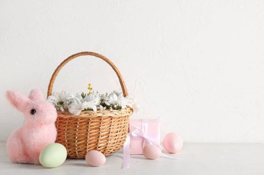 Dekoratif tavşan, hasır sepet, çiçekler ve beyaz grunge arka planda Paskalya yumurtaları.