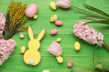 Paskalya yumurtaları, dekoratif tavşan ve yeşil ahşap arka planda çiçekler.