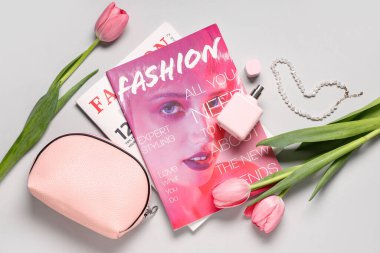 Pembe laleli dergiler, kozmetik çanta ve beyaz arka planda parfüm şişesi.