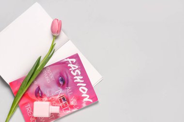 Pembe lale ve beyaz arka planda parfüm şişesi olan dergiler.