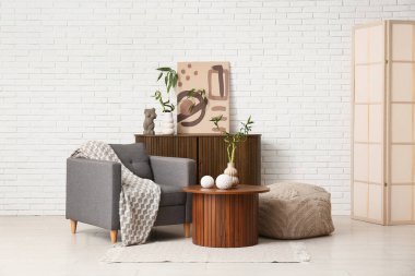 Bambu saplı ahşap masa, dekor, şık koltuk, puf ve poster hafif tuğla duvarın yanındaki dolapta.