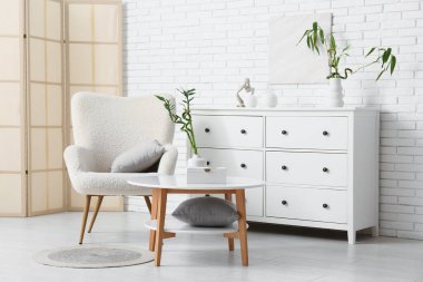 Masada bambu saplı vazo, hafif tuğla duvarın yanında şık koltuk ve çekmeceler.