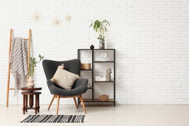 Şık koltuk, dekorlu raf ünitesi, bambu sapları ve hafif tuğla duvarın yanındaki merdiven.