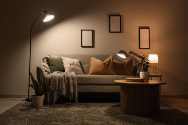 Geceleri karanlık oturma odasının içinde kanepe, masa ve parlayan lambalar var.