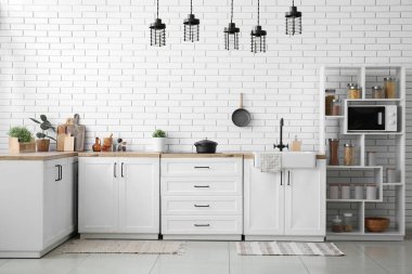 Mutfağın içinde beyaz tezgah, raf ünitesi ve çatal bıçak takımı var.