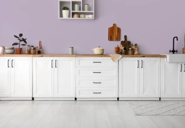 Mutfaktaki leylak duvarın yanında soba ve çatal bıçak bulunan beyaz tezgahlar.