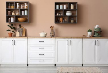 Mutfağın içi beyaz tezgahlar, raflar ve çatal bıçaklarla dolu.