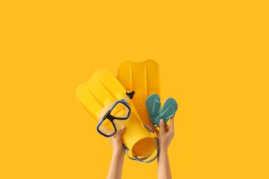 Sarı arka planda plaj aksesuarları olan kadın eller.