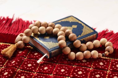 Beyaz ahşap arka planda tasbih ve dua halısı olan Kur 'an, yakın plan. Ramazan kutlaması