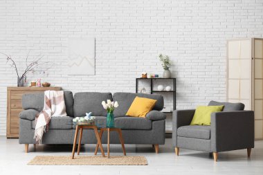 Şenlikli oturma odasının içinde şık gri kanepe, koltuk, kahve masası ve Paskalya süslemeleri.