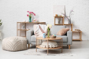 Şenlikli oturma odasının içinde şık gri kanepe, ahşap sehpa ve Paskalya süslemeleri var.