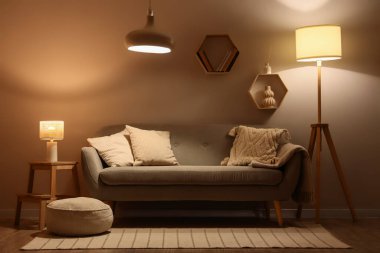 Modern oturma odasının içinde rahat kanepe, puf ve parlayan lambalar.